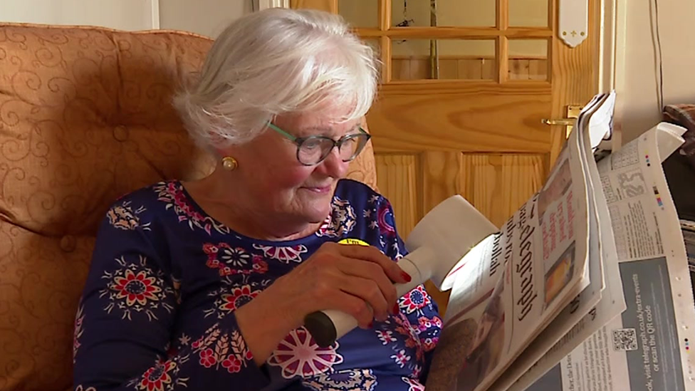 Pam Maxwell using a reading device with her newspaper because she has eyesight deterioration