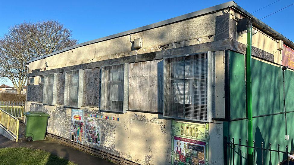 The exterior of the original building which is a single-storey concrete structure with grills over the windows and paintings on the outside wall