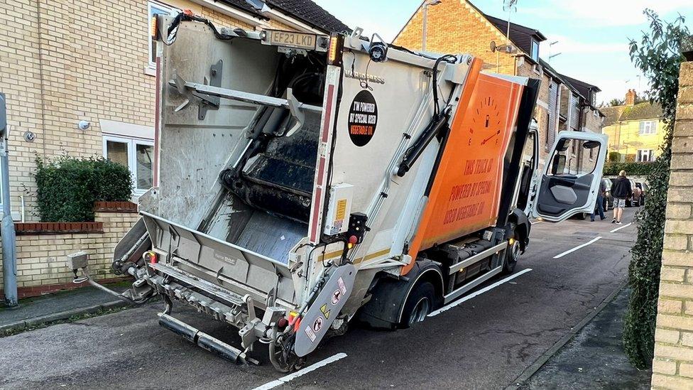 A bin lorry stuck in a hole in the road