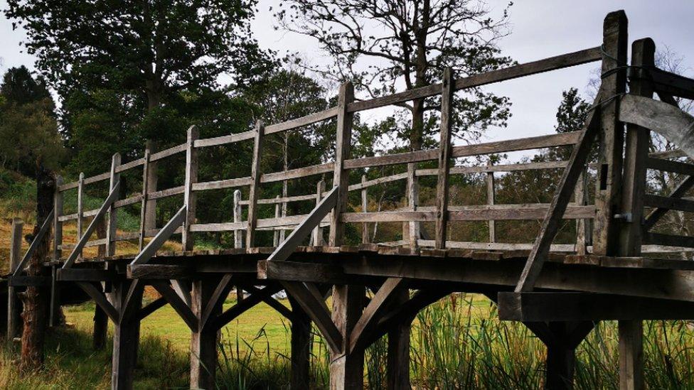 Side angle view of rebuilt wooden bridge in a field over water