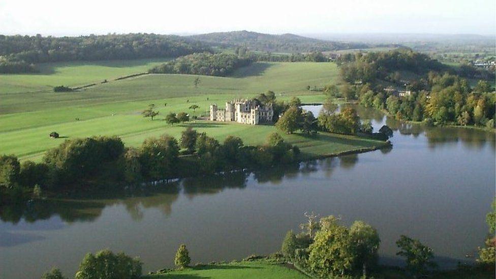 Sherborne Castle amid rolling green hills with a large expanse of water in front