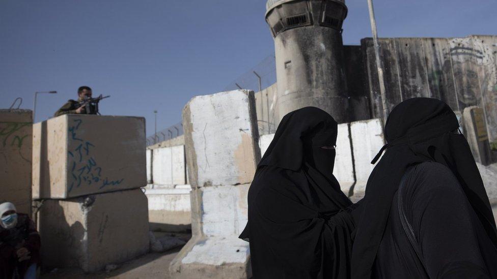 An Israeli soldier watches as Palestinians women wait to cross Qalandia checkpoint to attend the first Friday prayer service of Ramadan at the al-Aqsa Mosque in occupied East Jerusalem (16 April 2021)