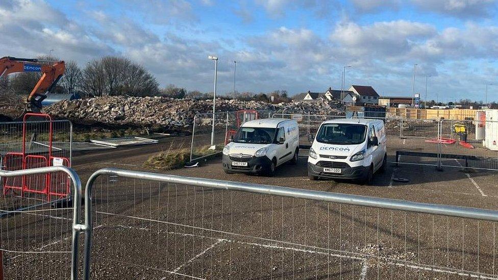 Contractors vans parked next to pile of demolition rubble.