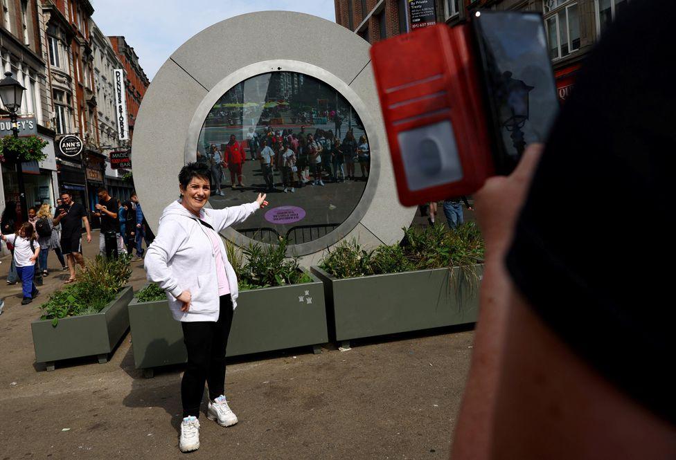 A woman poses in front of The Portal, a public technology sculpture that links with direct connection between Dublin, Ireland and the Flatiron district in Manhattan, New York City, in Dublin, Ireland, May 21, 2024.