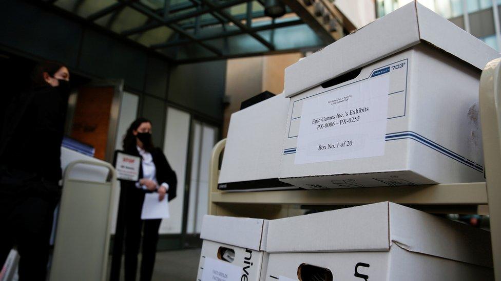 Boxes of documents wait outside a court building under guard - one label reads "Epic Games Inc's exhibits, box 1 of 20"