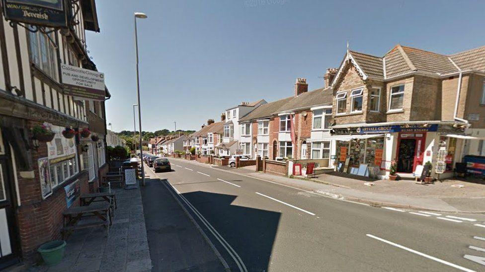 Sloping road with shops and homes on both sides, the street is in shade on the left and in sunshine on the right