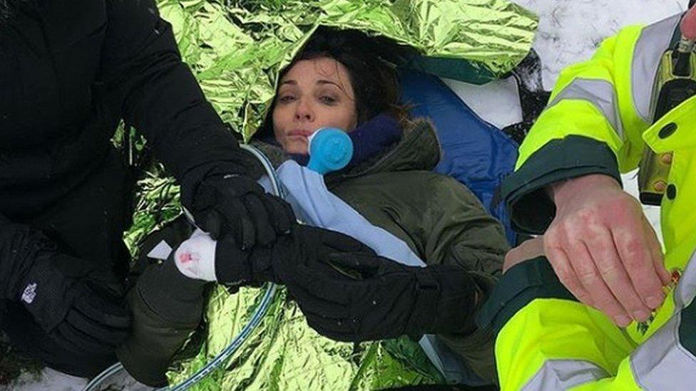 Actress Sarah Parish laying on the snow under a foil blanket and being treated by paramedics