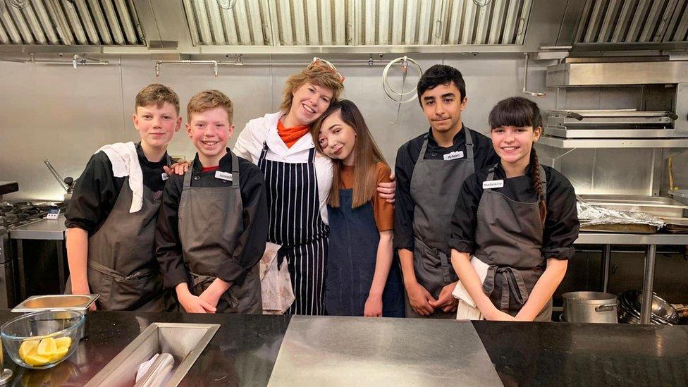 Picture of Nikki Lilly with contestants in aprons in the kitchen