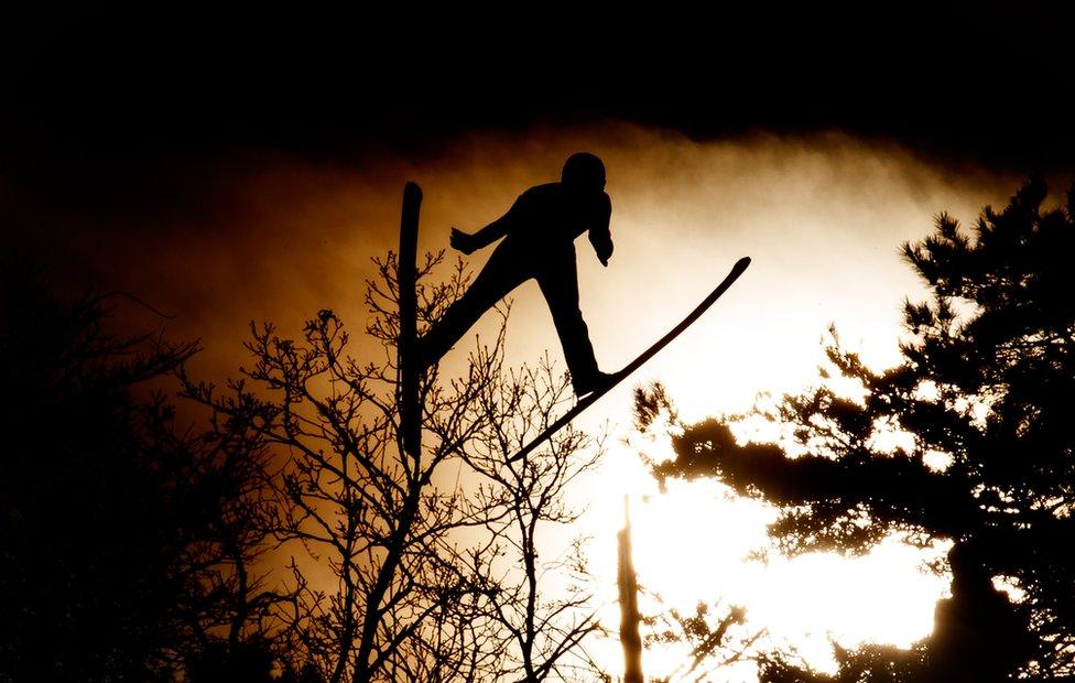 silhouetted figure jumping with skis