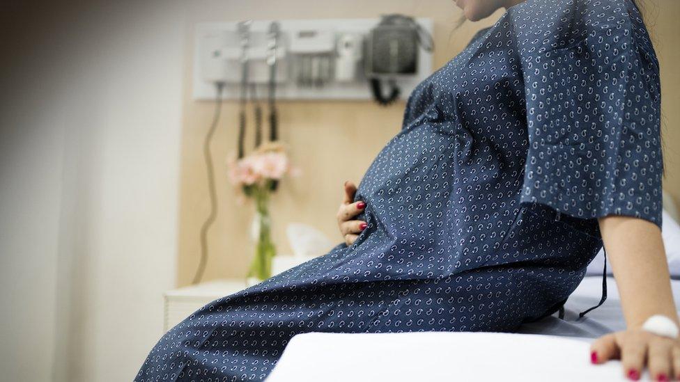 Pregnant woman in a gown sitting on a hospital bed