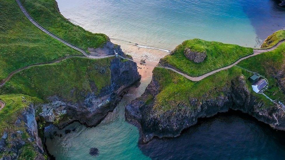 The rope bridge connecting the two cliffs in Northern Ireland it is called the Carrick-a-Rede Rope Bridge taken in an aerial shot