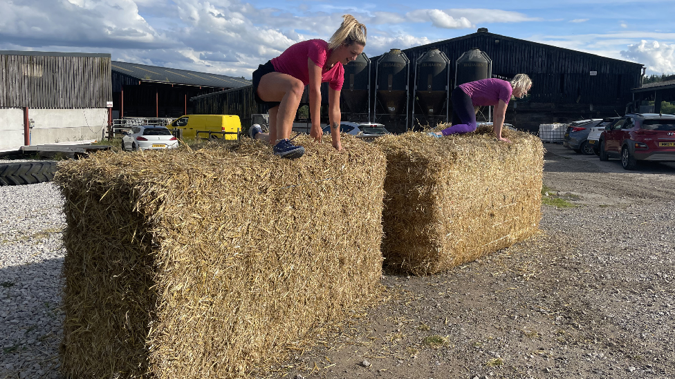 Two women climbing over hay bales