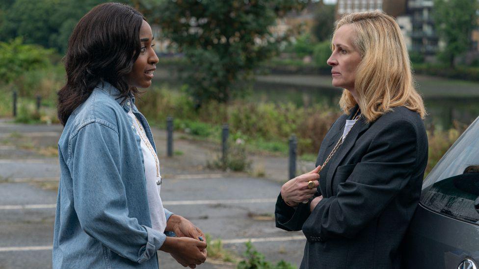 Ayo Edebiri and Julia Roberts standing outside facing each other, Roberts leaning on a car