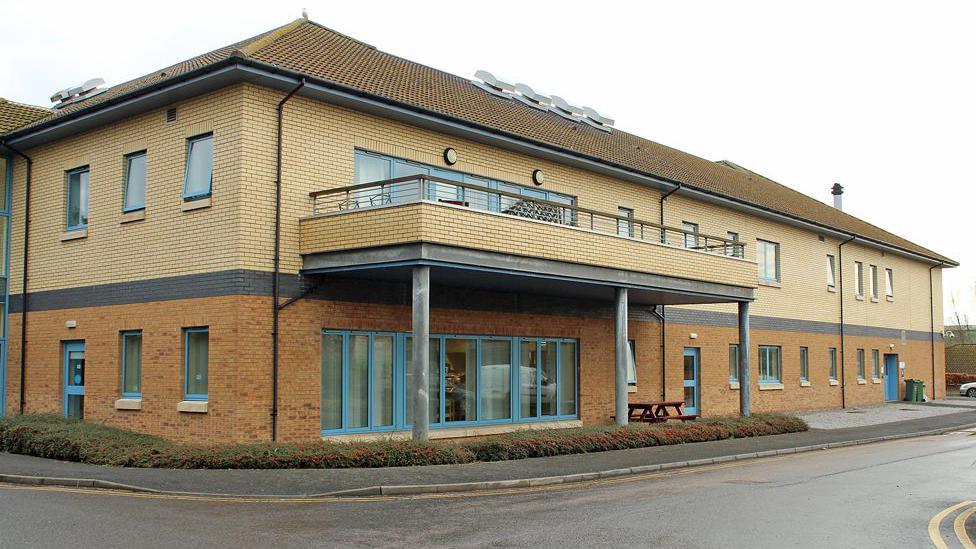 A hospital building in two shades of brick pictured on a grey day