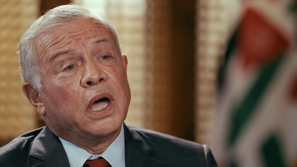 Jordan's King Abdullah, wearing a black suit jacket, pale blue shirt and red tie, speaks with his mouth open