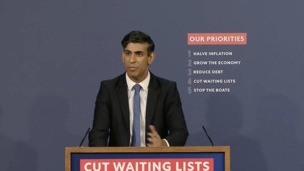 Rishi Sunak next to a board of pledges.