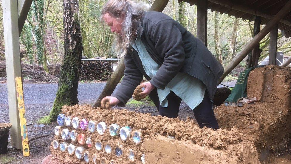 Lizzie Wynn building an ecobrick wall using cob, a mud and straw mix