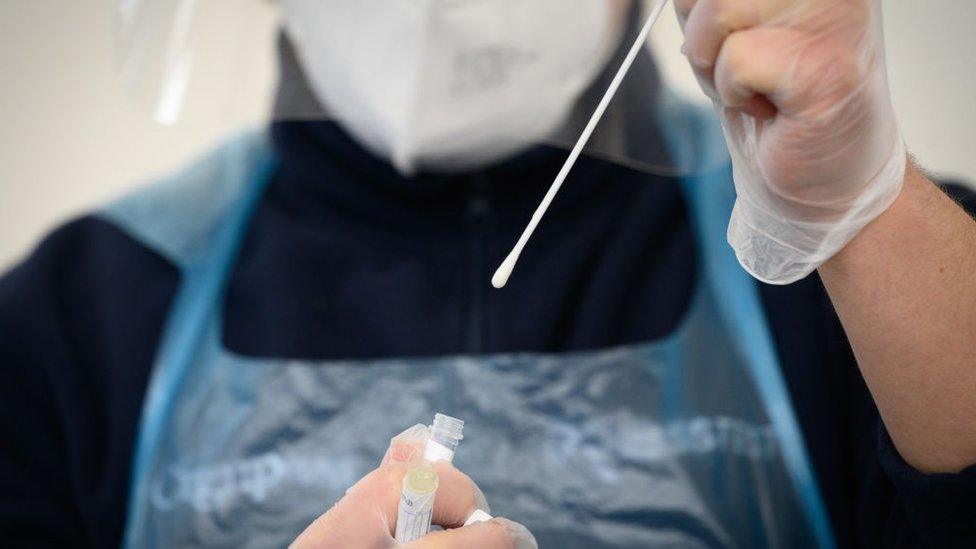 A member of the medical team holds up a used swab from a PCR test at Gatwick Airport