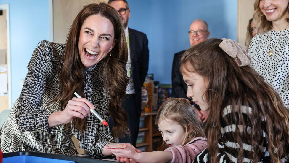 The Princess of Wales laughing as she paints a young girl's hand