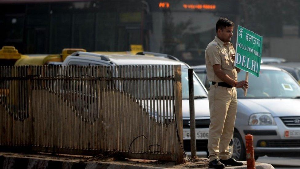 A Delhi civil defence personnel holds a placard bearing a "pollution-free Delhi" slogan at a traffic intersection in the Indian capital New Delhi on December 31, 2015