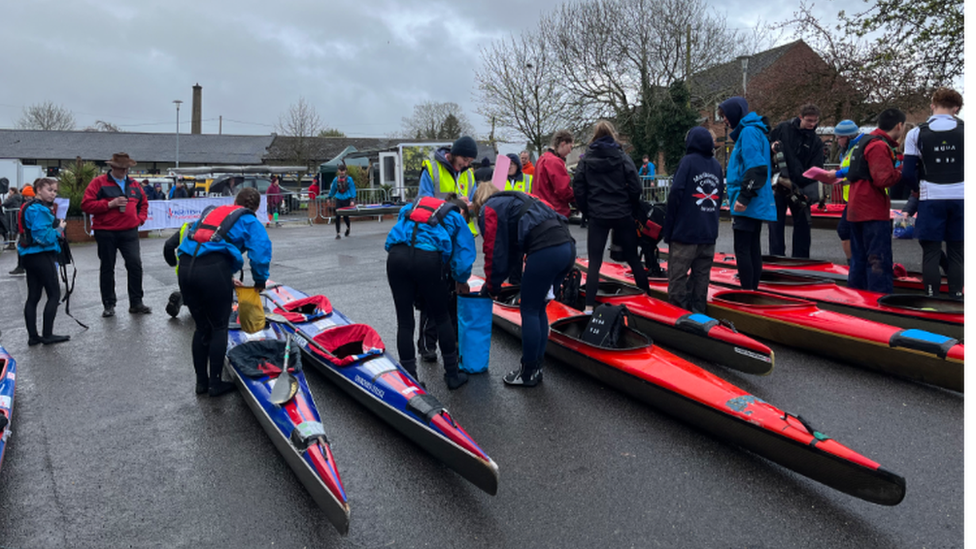 Canoeists wearing wetsuits and lifejackets carry out checks on their canoes and kit