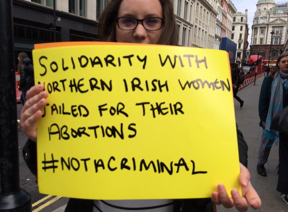 Woman holding a placard reading: "Solidarity with Northern Irish women jailed for their abortions #notacriminal"