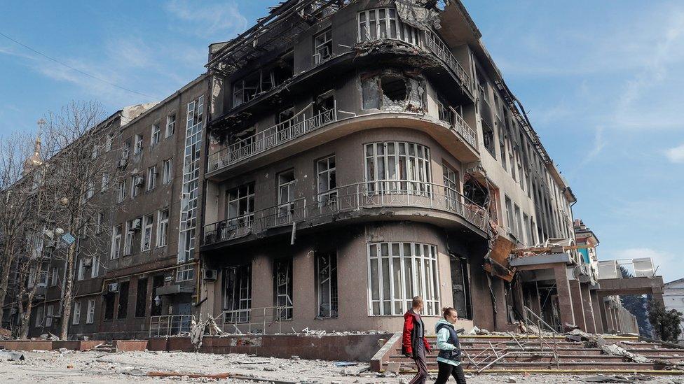 Residents walk past a destroyed building in the Ukrainian city of Mariupol