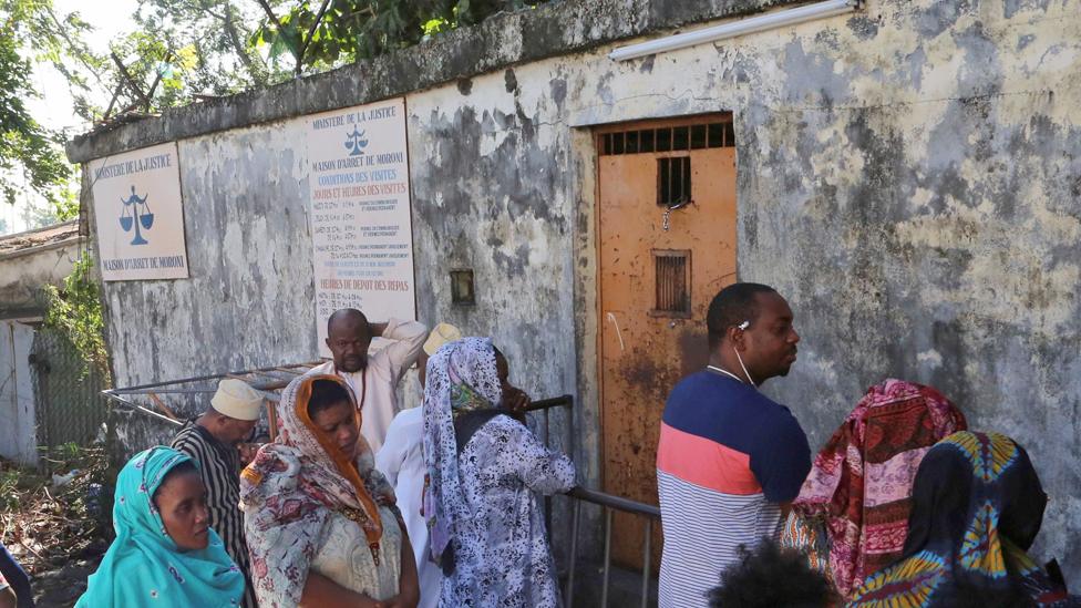 Relatives of prisoners wait outside the entrance to the main prison in Moroni, Comoros - 2019