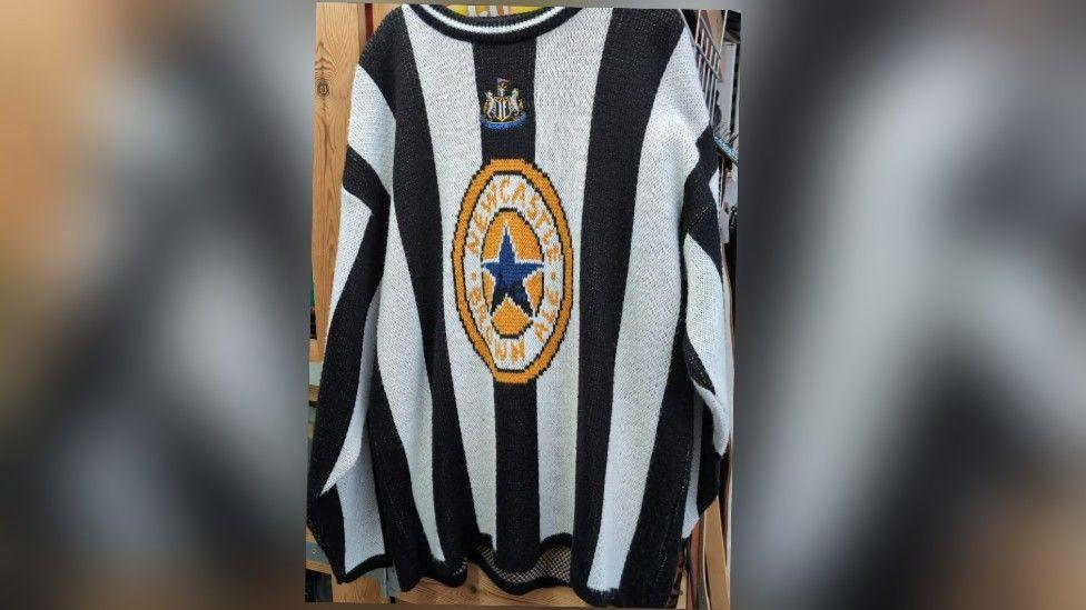 A Newcastle knitted jumper which is black and white with the Newcastle Brown Ale logo on the front 