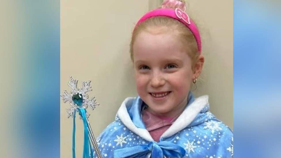 Casey, who has long blonde hair, wears a princess cape and holds a toy magic wand.