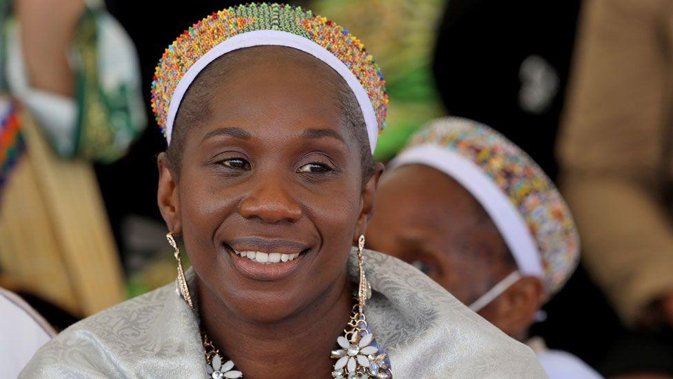 Queen Nozizwe kaMulela in a beaded headdress and wearing elaborate flower earrings and brocade grey silk-like brocade scarf.