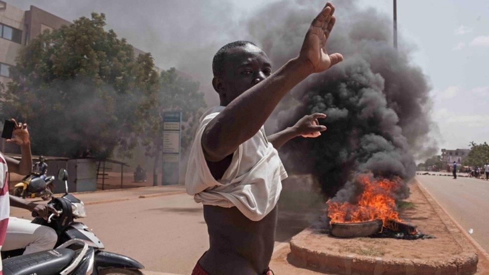 A Burkina Faso protestor gestures in front of burning tires as he and others take to the streets in the city of Ouagadougou, Burkina Faso, Thursday, 17 September 2015