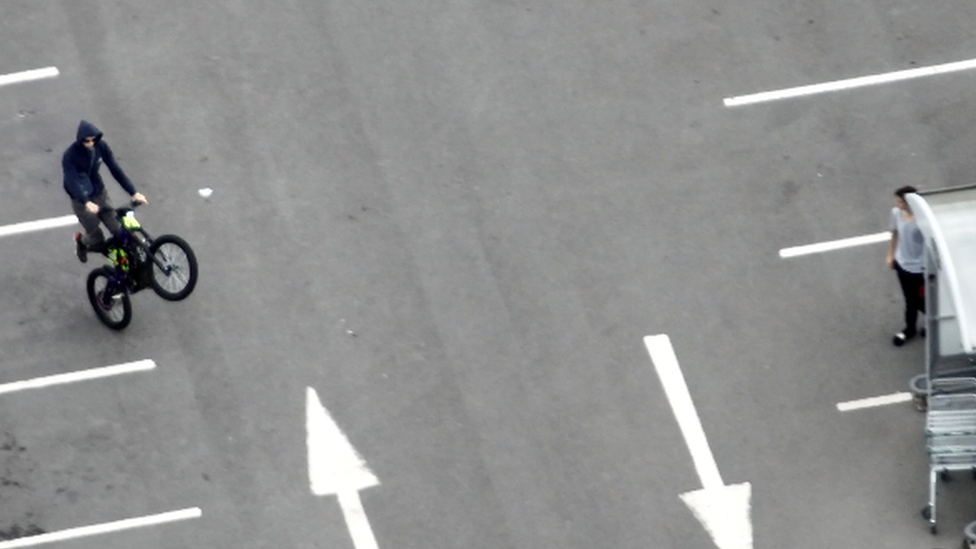 Man on electric motorbike does a wheelie in a car park