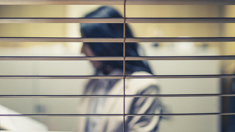 A woman in an office behind window blinds