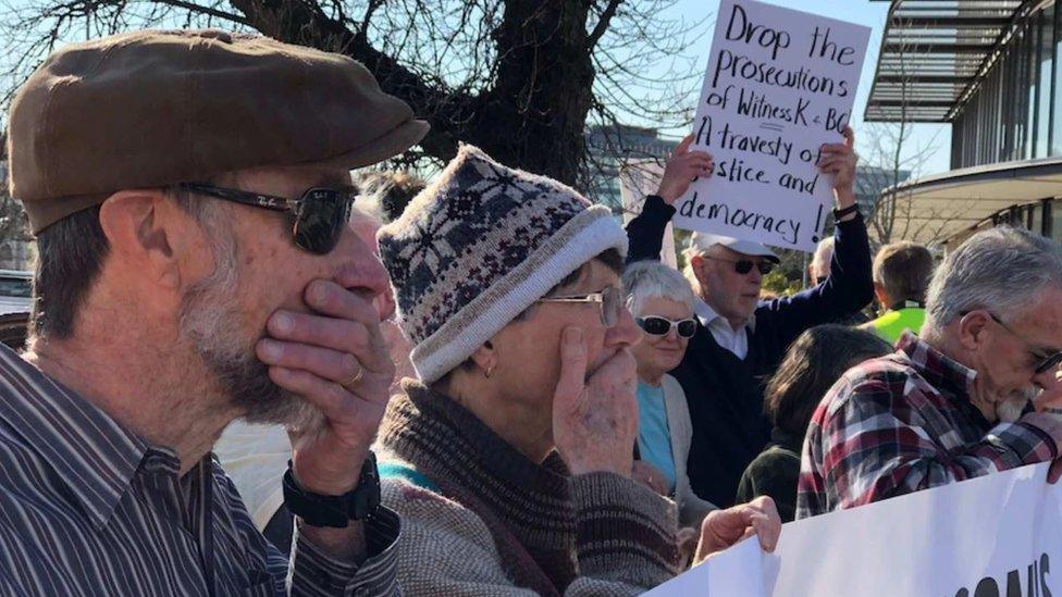 Protestors cover their mouths at a demonstration protesting the prosecution of Bernard Collaery