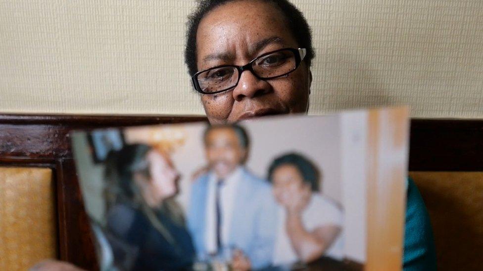 A woman holding up a photo of three people, presumably family members