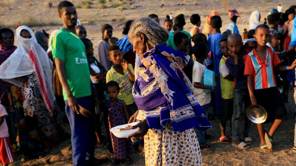 An Ethiopian woman who fled war in the northern Tigray region carries her food ration as others queue at the Um-Rakoba camp on the Sudan-Ethiopia border, Sudan, 19 November 2020