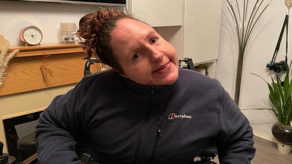 Georgina Moore smiling at the camera, sitting in her wheelchair at home