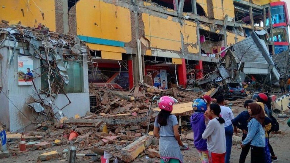 People stand in front of a damaged shopping mall in Palu