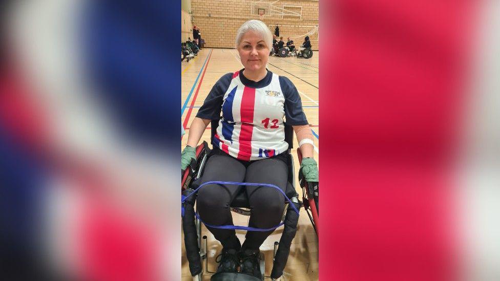 Joanne Whyatt seen sitting in a wheelchair wearing her Team UK rugby kit which comprises of a white T-shirt with navy blue sleeves and a Union Flag pattern on the front.