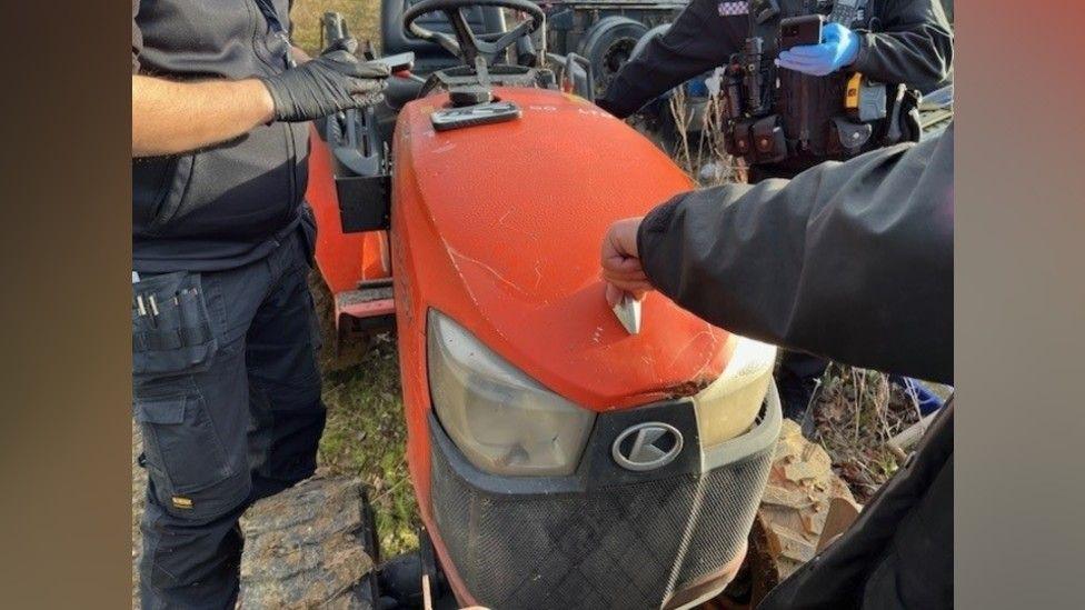 A red tractor. There are three police officers also in the picture wearing black police uniform and gloves. 