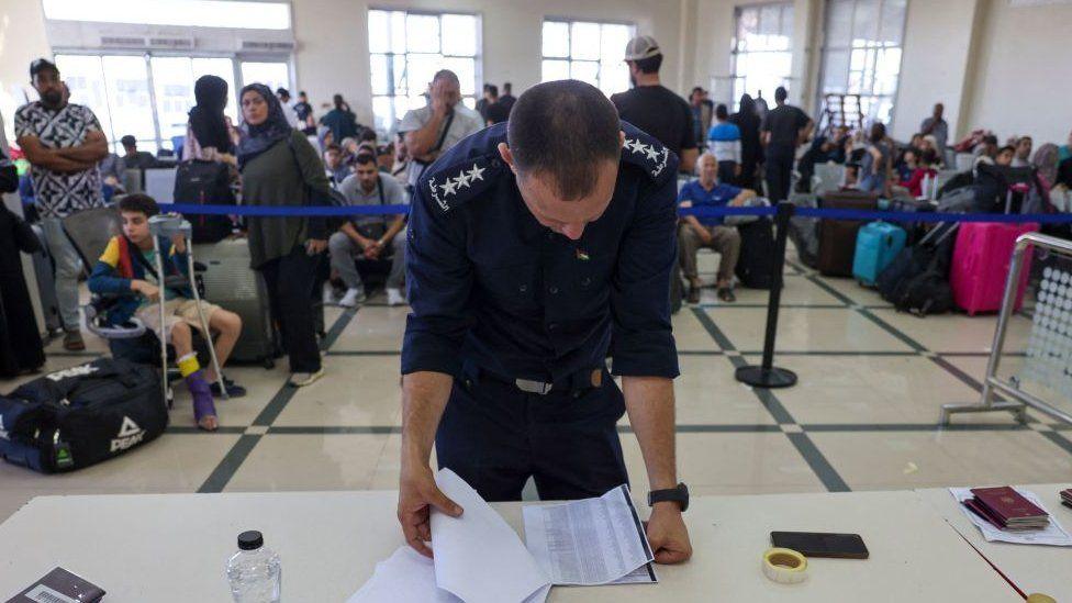A Palestinian border guard checks the documents of dual nationals and foreigners as they wait to cross the Rafah border crossing with Egypt, in the southern Gaza Strip, on November 7, 2023