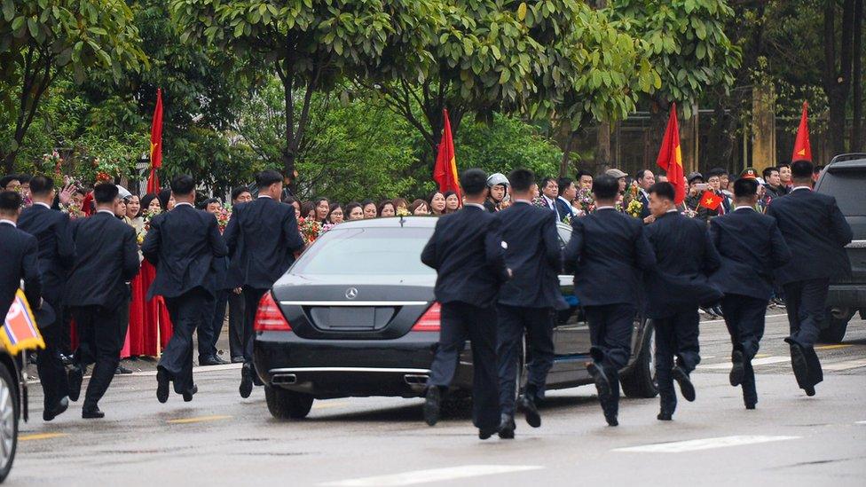 Bodyguards running next to a limousine