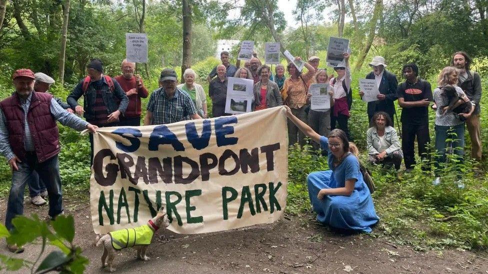 Campaigners gather in a forest holding placards to keep Grandpont Nature Park