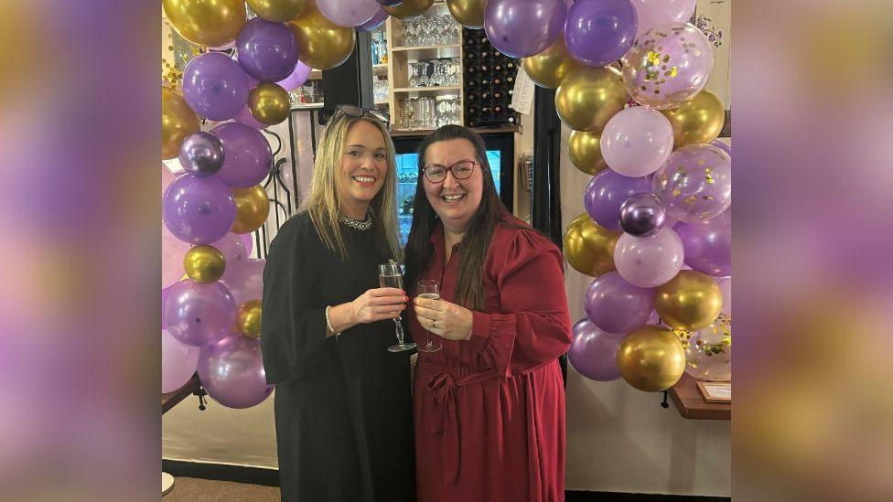 Two women stood under loads of balloons