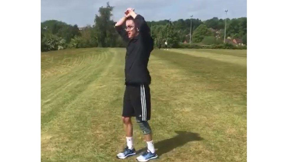 Tom in a green field with his hands in the air, following a run uphill