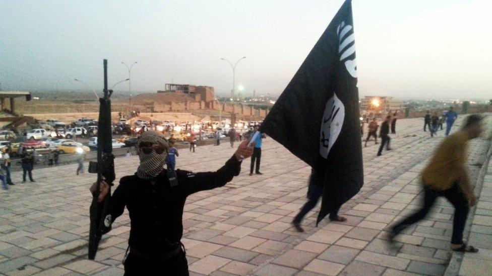 A fighter of the so-called Islamic State group holds an IS flag and a weapon on a street in the city of Mosul, Iraq, on 23 June 2014