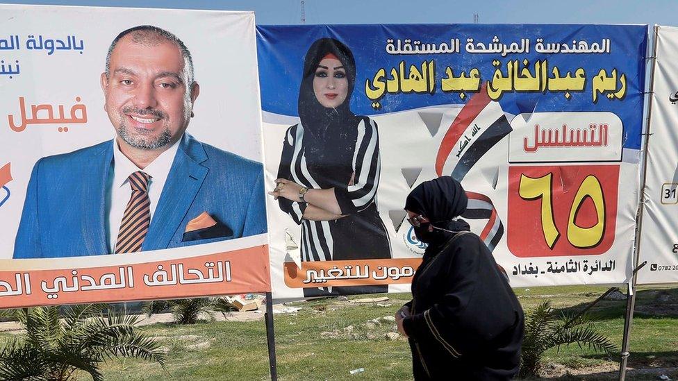 An Iraqi woman walks next to election campaign posters for candidates in Baghdad, Iraq (5 October 2021)