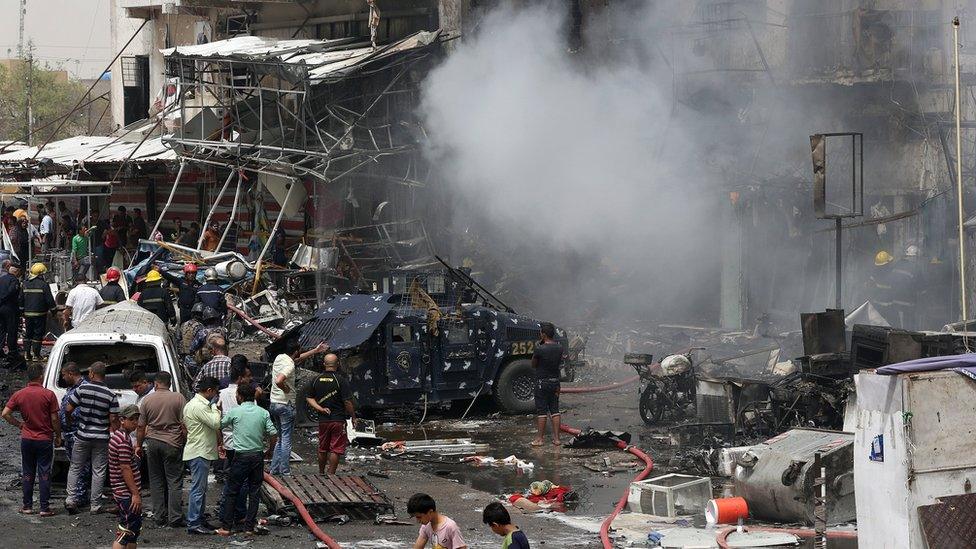 Smoke rises as Iraqi security forces and civilians gather at the scene of a deadly suicide car bomb attack in Baghdad on 9 June