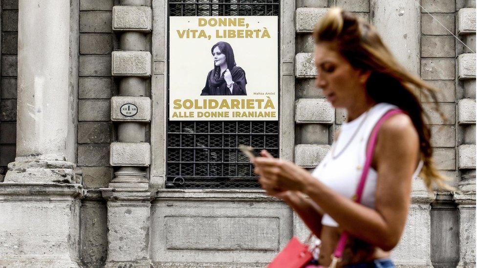 A woman walks in front of a portrait of Mahsa Amini displayed on the facade of Palazzo Marino, in Milan, Italy